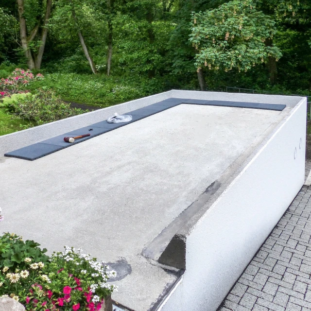 Płyty tarasowe WARCO w szarym kolorze są układane na betonowym dachu garażu obok budynku mieszkalnego, aby przekształcić dach w komfortowy taras.