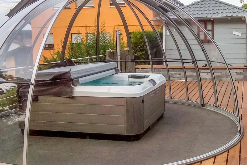 Na drewnianym tarasie z półotwartą wiatą znajduje się jacuzzi z hydromasażem ustawione na antypoślizgowych płytach basenowych WARCO.