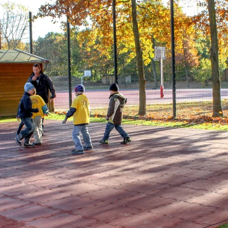 Boisko sportowe w szkole, wyposażone w czerwone płyty boiskowe WARCO, które zapewniają ochronę w razie upadku oraz precyzyjne odbicie piłki.