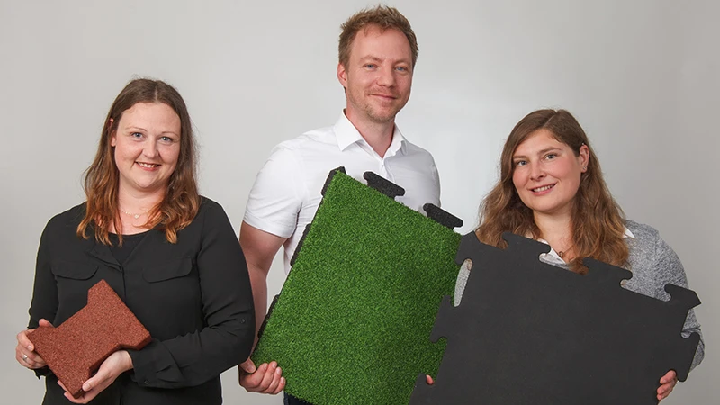 Z życzliwym uśmiechem trzech konsultantów WARCO prezentuje płyty wykonane z poliuretanowo wiązanego granulatu gumowego w kolorach brązowym, zielonym i czarnym. Zaprojektowane z myślą o balkonach, zapewniają antypoślizgową i wytrzymałą powierzchnię. Każda wersja ma unikalny wzór i łatwo się ją układa. Dzięki specjalistycznej wiedzy ekspertów wybierzesz idealne pokrycie na bezpieczny i estetyczny balkon. Płyty są proste w pielęgnacji i oferują wysoki komfort.