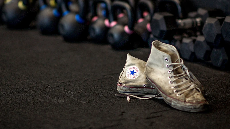 Zużyte trampki Converse leżą na czarnych sportowych matach ochronnych WARCO w siłowni z hantlami.