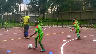 Grupa nastolatków z wielkim entuzjazmem gra w piłkę nożną na zewnętrznym boisku wykonanym z czerwonych płyt WARCO.