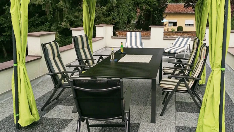 Na tarasie dachowym znajduje się nawierzchnia z płyt tarasowych WARCO o jasnoszarej i ciemnoszarej, marmurkowej tonacji przypominającej granit. Baldachim chroni kącik wypoczynkowy na elastycznej, odpornej na warunki atmosferyczne powierzchni. Płyty antypoślizgowe i amortyzujące można ułożyć bez trwałego klejenia, co dodatkowo tłumi odgłosy kroków. W efekcie powstaje łatwa w utrzymaniu przestrzeń, doskonała do relaksu na świeżym powietrzu.