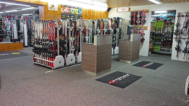 Za dwoma ladami w sklepie narciarskim Gaby Sports znajdują się stoiska z różnymi modelami nart. Podłoga pokryta jest płytami na zatrzask WARCO w kolorze Maroko.