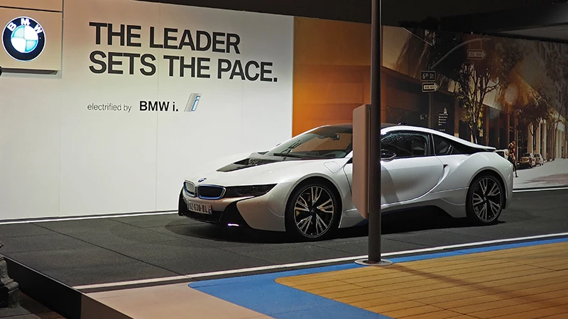 Samochód BMW i8 jest prezentowany na targach. Sportowy samochód stoi na czarnej podłodze wystawowej WARCO, która swoim wyglądem przypomina asfaltową ulicę.