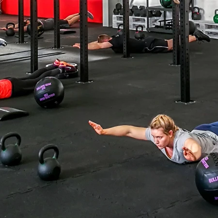 Ludzie leżą na ciemnej, elastycznej podłodze w sali gimnastycznej. Podłoga wykonana jest z mat sportowych WARCO.