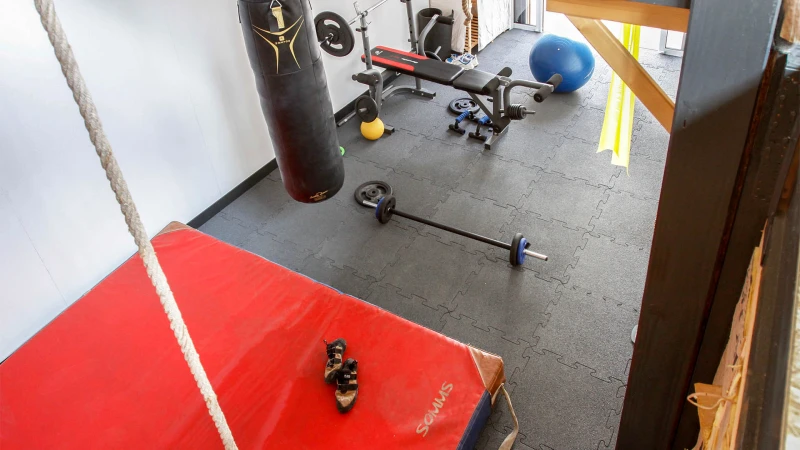 W prywatnej domowej siłowni, na szarych sportowych matach ochronnych WARCO w kształcie puzzli, które chronią stawy, tłumią wibracje i izolują, znajdują się różne sprzęty do treningu siłowego