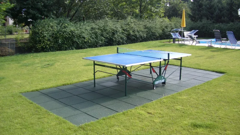 Pod stołem do tenisa stołowego w ogrodzie znajduje się podłoga sportowa wykonana z zielonych płyt amortyzujących WARCO.
