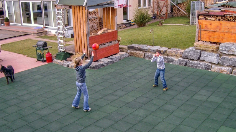 Kobieta i chłopiec grają w siatkówkę na przydomowym boisku wykonanym z zielonych płyt WARCO w ogrodzie.