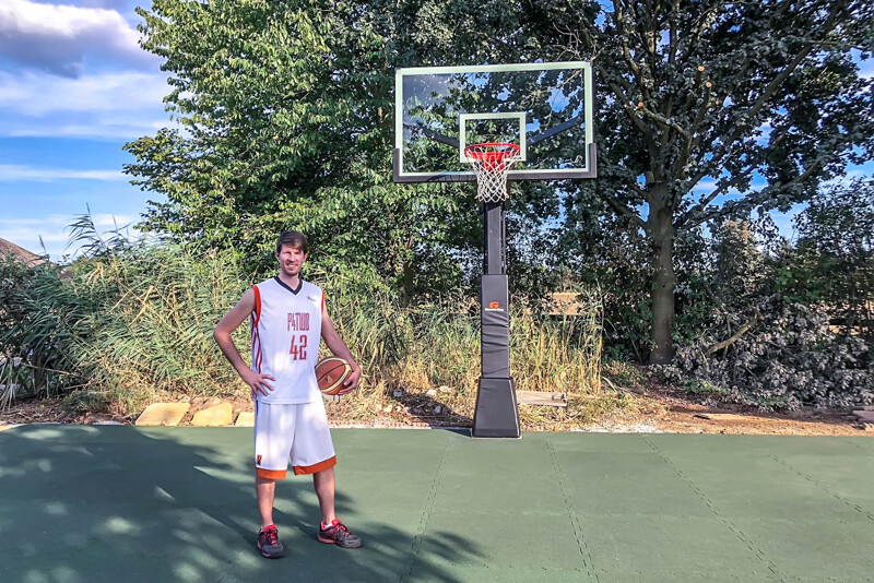 Na boisku do koszykówki w ogrodzie z płytkami boiskowymi WARCO, znajduje się koszykarz.