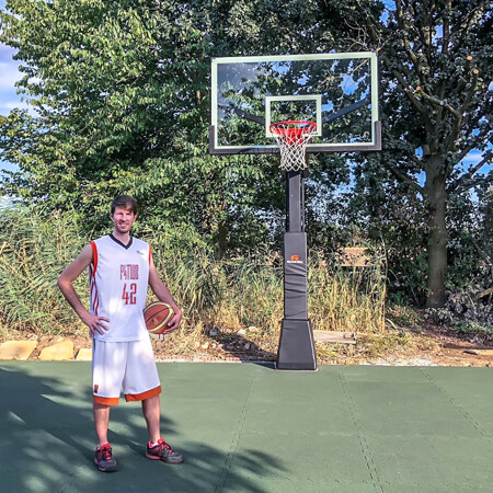 Na boisku do koszykówki w ogrodzie z płytkami boiskowymi WARCO, stoi profesjonalny koszykarz.