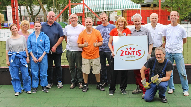 Pod koniec pracy zespół Zentis ustawia się do pamiątkowego zdjęcia. Kobiety i mężczyźni stoją na gumowej podłodze eventowej WARCO w kolorze zielonym.