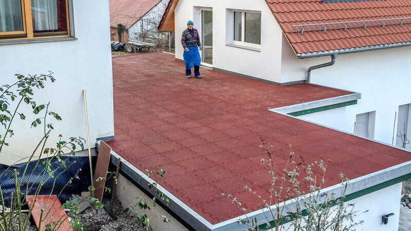 Na płaskim dachu garażu, który został wybudowany pomiędzy dwoma domami, zostały ułożone czerwone płyty tarasowe WARCO.
