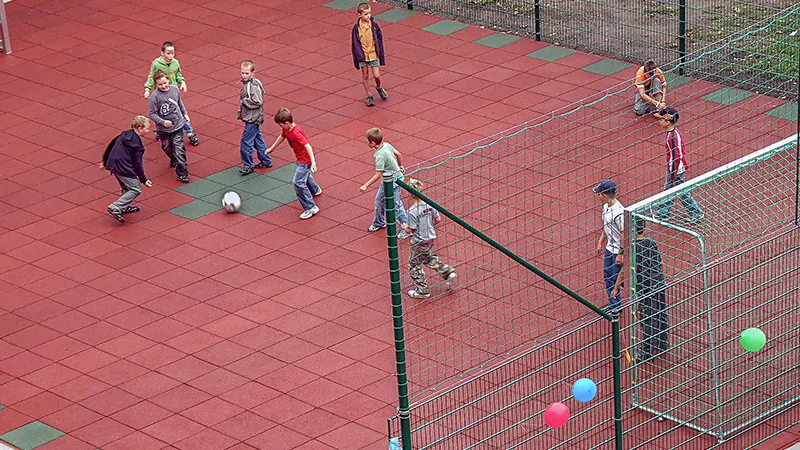 Dzieci grają w piłkę nożną na nowym boisku szkolnym wykonanym z czerwonych i zielonych płyt WARCO.