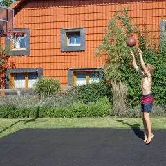 Małe boisko do koszykówki w ogrodzie wykonane z płyt boiskowych WARCO w kolorze antracytu zostało stworzone przez rodzinę. Chłopiec gra w koszykówkę.