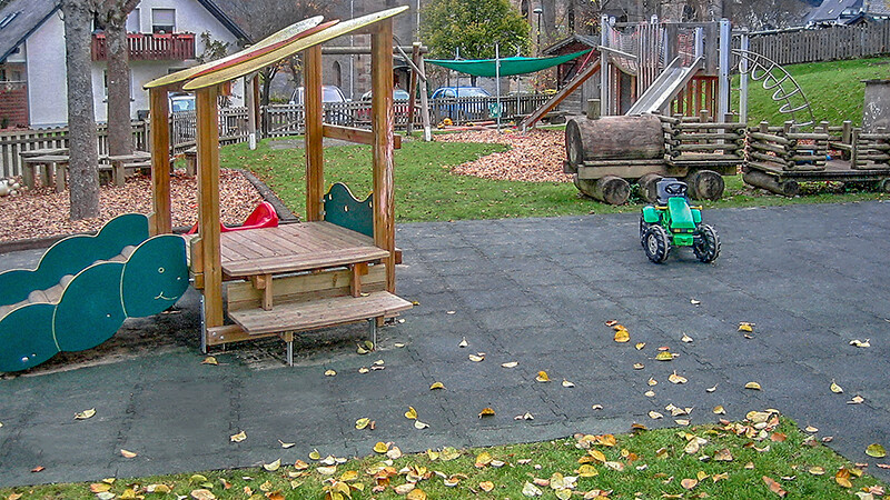 Naturalny plac zabaw w Olsbergu wykonany z szarych, amortyzujących upadki płyt WARCO z  drewnianym domkiem do zabawy.